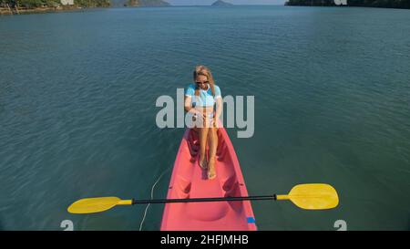 Donna piuttosto sottile in elegante costume da bagno giace in kayak di plastica rosa che scivolano sull'oceano azzurro a vista esotica resort superiore. Foto Stock