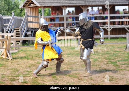 Due cavalieri combattono in armatura con spade, ricostruzione del torneo. Una scena con spettatori da una casa di tronchi. Celebrazione della pagana da Foto Stock