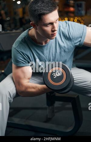 Giovane uomo muscolare focalizzato che fa bicep arricciatura Foto Stock