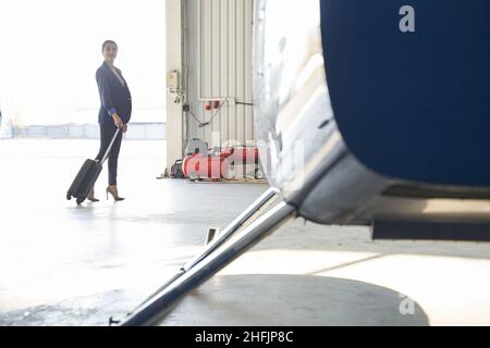 Donna elegante con valigia carrello in piedi nel hangar aereo Foto Stock