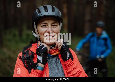 Motociclisti senior che mettono il casco da ciclismo all'aperto nella foresta in autunno giorno, guarda la macchina fotografica Foto Stock