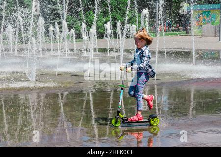 Ucraina - 26 maggio 2018. Una ragazza guida uno scooter in una pozzanghera accanto alla fontana. Foto Stock