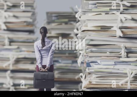 Frustrato donna d'affari persa che fissava a mucchi enormi di lavoro cartaceo, sovraccarico di lavoro e concetto di burocrazia Foto Stock