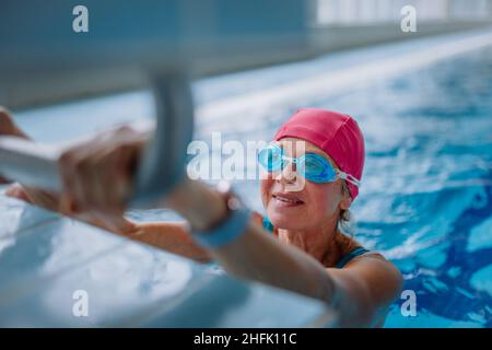 Nuotatore donna anziano attivo che tiene sul blocco di partenza preparandosi a nuotare nella piscina interna. Foto Stock