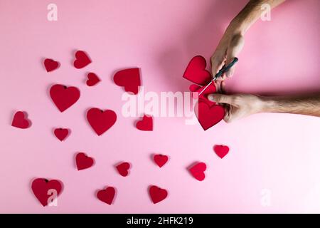 Guy prepara il cuore rosso con carta su sfondo rosa Foto Stock