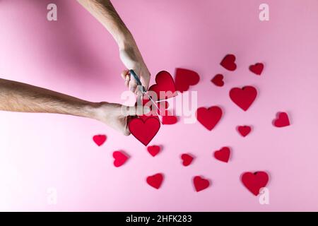 Guy prepara il cuore rosso con carta su sfondo rosa Foto Stock