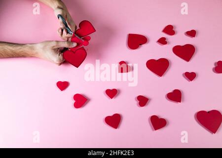 Guy prepara il cuore rosso con carta su sfondo rosa Foto Stock