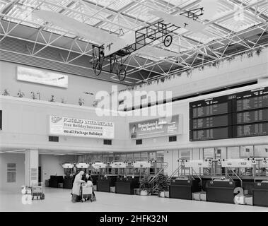 Aeroporto di Birmingham, Birmingham Maglev, Elmdon, Birmingham, Bickenhill, Solihull, 23/01/1985. L'interno del pozzo centrale nel nuovo edificio del terminal dell'aeroporto internazionale di Birmingham dopo la sua apertura, mostrando i passeggeri di fronte a una fila di banchi per il check-in. La costruzione di un nuovo edificio terminale e dei moli, le estensioni alle piste e un nuovo sistema Maglev all'aeroporto di Birmingham è iniziata nel maggio 1981. Il nuovo edificio del terminal si trova sul lato opposto del sito al terminal esistente di Elmdon. E 'stato costruito utilizzando un telaio in acciaio strutturale intorno ad un pozzo centrale, con pavimento prefabbricato AN Foto Stock