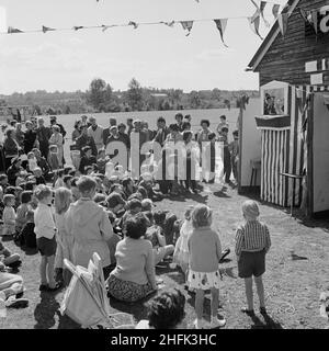 Laing Sports Ground, Rowley Lane, Elstree, Barnet, Londra, 26/06/1965. I bambini assistono a uno spettacolo di punch e Judy durante l'annuale giornata di sport di Laing che si tiene presso il Laing Sports Ground di Elstree. Nel 1965 la giornata sportiva annuale di Laing si è svolta presso il campo sportivo di Rowley Lane il 26th giugno. Oltre al calcio e all'atletica, sono stati organizzati eventi di novità, tra cui la gara di sacchi e Donkey Derby, ed eventi per bambini, tra cui gare di go-kart, gare di abbigliamento fantasioso e corse di pony. Foto Stock