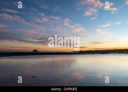 North Berwick, East Lothian, Scozia, UK, 17th gennaio 2022. UK Meteo: alba sul Firth of Forth con la Bass Rock sull'orizzonte marino e le nubi rosa dell'alba riflesse nell'acqua di mare della piscina marea Foto Stock