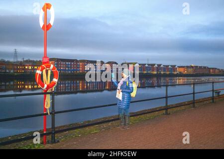 Preston, Lancashire. Meteo Regno Unito. 17 Jan 2022. Kathy una guida locale di Weight Watchers che tiene un tablet o una camma di trekking, sta effettuando una passeggiata mattutina virtuale o un tour guidato Zoom intorno a Prestons banchine per i suoi 200 membri snellenti del club, che a causa delle normative Covid stanno facendo una passeggiata simulata a casa. Mentre il viaggio si è quasi fermato durante la pandemia del coronavirus, la tecnologia ci permette di visitare quasi ogni posto del pianeta in un batter d'occhio. Credit: MediaWorldImages/AlamyLiveNews Foto Stock