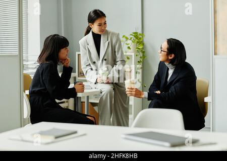 Gruppo di giovani uomini d'affari asiatici che chiacchierano durante la pausa caffè all'interno dell'ufficio Foto Stock