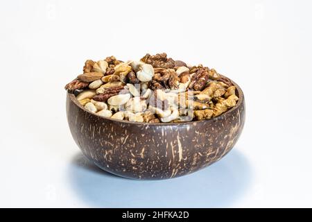 Le noci si mescolano in una ciotola di legno di cocco su uno sfondo bianco Foto Stock