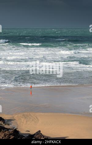 La piccola figura di persona che corre lungo la costa su una ventosa Fistral Beach a Newquay in Cornovaglia. Foto Stock