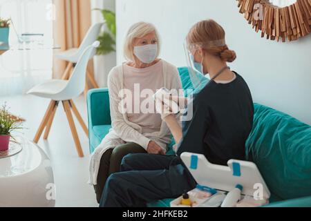 Donna anziana visitata da infermiera distrettuale a casa Foto Stock
