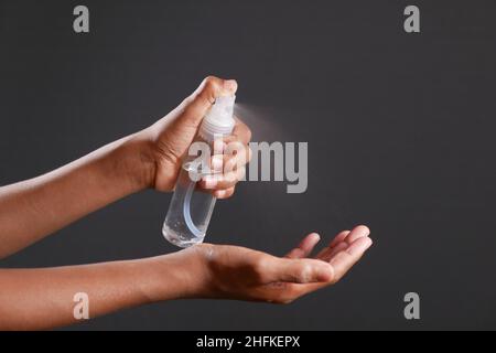 primo piano della mano del giovane uomo usando lo spray disinfettante per le mani isolato su nero Foto Stock