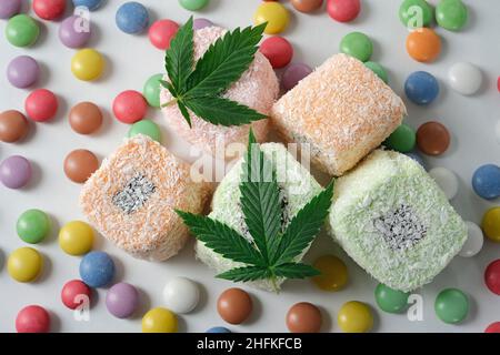 Cannabis alimentare. Delizia turca con fiocchi di cocco e confetti colorati da vicino. Foglie verdi di cmarijuana su sfondo bianco. Disposizione della canapa f Foto Stock