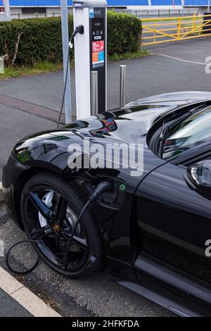 Porsche Taycan 4S auto elettrica collegata a un punto di ricarica nel parcheggio NEC, Birmingham, Inghilterra Foto Stock