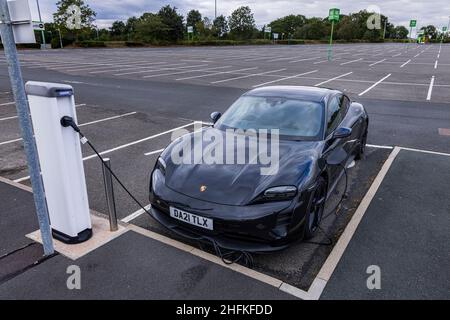 Porsche Taycan 4S auto elettrica collegata a un punto di ricarica nel parcheggio NEC, Birmingham, Inghilterra Foto Stock