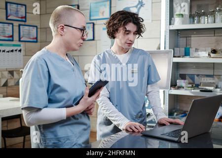 Medico maschile usando il computer e parlando con il suo collega, si discute momenti di lavoro in clinica veterinario Foto Stock