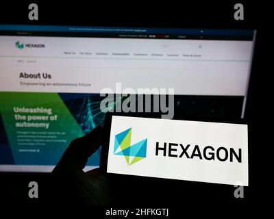 Persona che tiene lo smartphone con il logo della società di software svedese Hexagon AB sullo schermo di fronte al sito Web. Mettere a fuoco sul display del telefono. Foto Stock