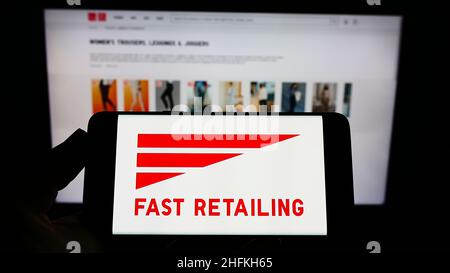 Persona che detiene il cellulare con il logo della società giapponese K.K. Fast Retailing sullo schermo di fronte al sito web Uniqlo. Mettere a fuoco sul display del telefono. Foto Stock