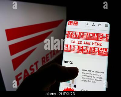 Persona che tiene lo smartphone con la pagina Web Uniqlo della società giapponese K.K. Vendita rapida su schermo con logo. Concentrarsi sul centro del display del telefono. Foto Stock