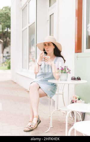 Estate. Bella giovane donna seduta in un caffè di strada e gusto gelato. Orientamento verticale. Foto Stock