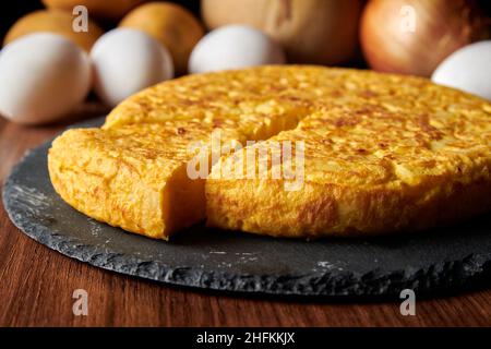 Un primo piano di una fresca e gustosa frittata spagnola e gli ingredienti sullo sfondo, un piatto tradizionale spagnolo Foto Stock