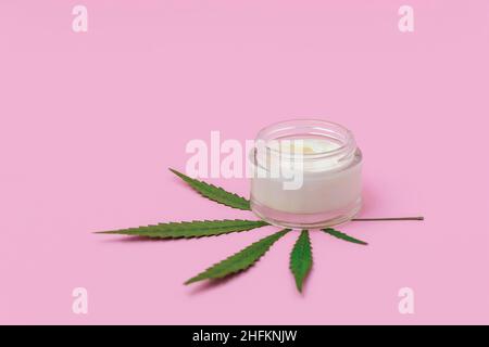 Crema di canapa di cannabis con foglia di marijuana su sfondo rosa morbido con spazio copia. Concetto di cosmesi infusi di cannabis Foto Stock