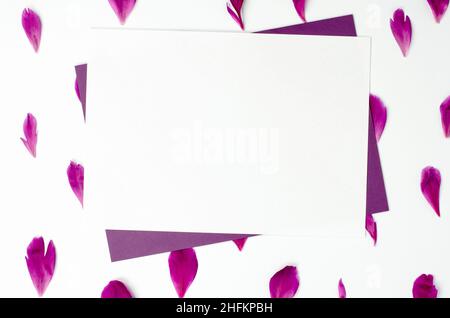 Un foglio bianco di carta su petali di peonia. Vuoto per un biglietto di auguri o un invito. Congratulazioni per le vacanze, spazio copia Foto Stock