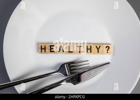 Piatto bianco con le parole sano e un punto interrogativo vista dall'alto con forchetta e coltello, salute medica e concetto di cibo Foto Stock