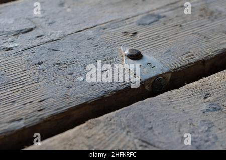 Numero 12. Una vecchia tavola con un'etichetta in alluminio. La barra di metallo è inchiodata al pavimento. Primo piano. Messa a fuoco selettiva. Foto Stock