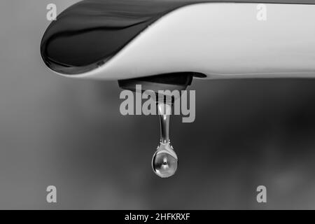 Goccia d'acqua cristallina che cade dal rubinetto. Fotografia in bianco e nero. Foto Stock