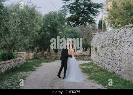 Felice coppia sorridente di stile che cammina in Toscana, Italia il giorno del matrimonio. La sposa e lo sposo camminano lungo la strada per le mani. Un giovane di stile Foto Stock