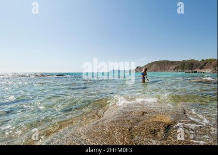 Giovane bella donna in piedi su rocce nelle acque cristalline dell'isola sarda. Foto Stock