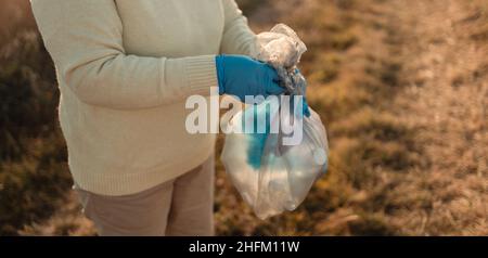 Giorno della terra. La mano dell'attivista femminile mette un sacchetto di plastica in un sacchetto della spazzatura. Ambiente inquinamento plastico Foto Stock