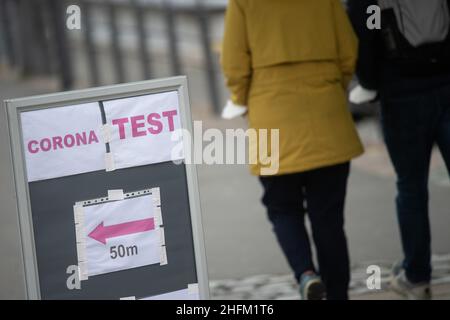 17 gennaio 2022, Hessen, Francoforte sul meno: Due persone camminano oltre un cartello che indica una stazione di prova di Corona. Francoforte fu il primo distretto in Assia a superare un'incidenza di sette giorni di nuove infezioni da Corona per 100.000 abitanti di 1000. Foto: Sebastian Gollnow/dpa Foto Stock