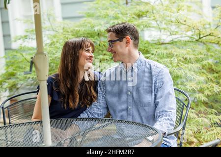 Acouple di un marito e di una moglie seduti sotto un tavolo ombrello esterno patio nel cortile Foto Stock