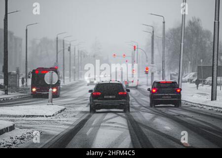 Vista prospettica artistica di una strada durante una tempesta di neve, con luci rosse da auto e semafori Foto Stock