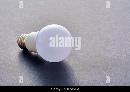 Una lampada LED bianca con base E27 giace su uno sfondo grigio Foto Stock