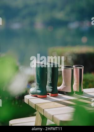 Il suo e il suo giardino stivali wellington che si asciugano nel primo sole estivo sul tavolo da giardino - rosa verde wellies coppia pensione stile di vita pensionato coppia wellies Foto Stock