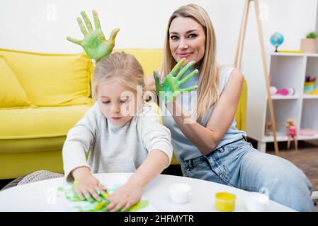 Donna che tiene le mani in vernice vicino capretto disegno a casa Foto Stock