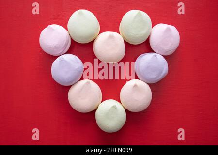 Forma del cuore da marshmallows pastello multicolore su sfondo di legno rosso. Dolce regalo per San Valentino. Dolci e cibo di sottofondo. Può essere utilizzato Foto Stock