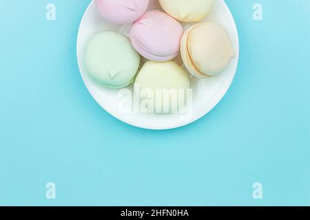 Mini marshmallows colorati assomiglia a macaroon in un piatto nero su uno sfondo blu pastello. Sfondo alimentare Foto Stock