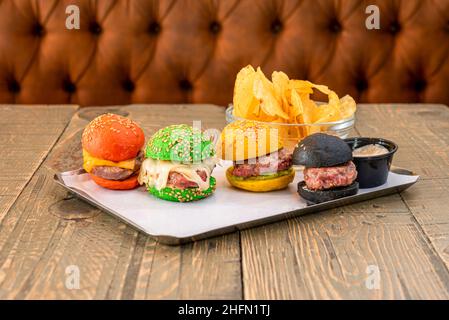 Mini hamburger di manzo con pancetta fritta e tacos di formaggio fuso e panini di diversi colori con una ciotola di patatine fritte Foto Stock