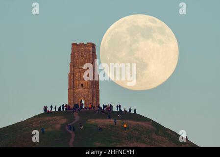 Glastonbury, Somerset, Regno Unito. 17th gennaio 2022. Meteo Regno Unito. La Luna piena del lupo si alza da dietro la St Michael’s Tower su Glastonbury Tor nel Somerset in una fredda serata limpida, mentre le persone si alzano in cima e la guardano crescere. Picture Credit: Graham Hunt/Alamy Live News Foto Stock