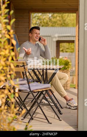 Uomo che parla su smartphone che si sta sedendo all'aperto Foto Stock