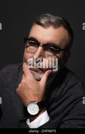 ritratto di uomo anziano serio in occhiali e orologio da polso guardando la telecamera isolata su grigio scuro Foto Stock