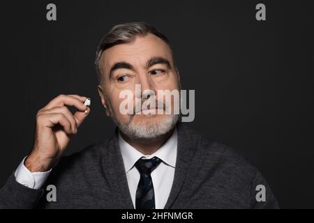 uomo anziano bearded in cravatta tenuta auricolare isolato su grigio scuro Foto Stock